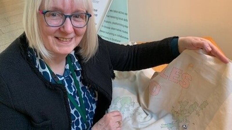 Beatrice Wishart shows a cloth with a map of Scotland on it with a button she sewed onto Shetland